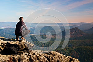 Climbing adult man at the top of rock with beautiful aerial view of the deep misty valley bellow