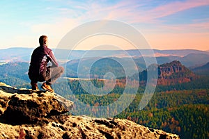 Climbing adult man at the top of rock with beautiful aerial view of the deep misty valley bellow