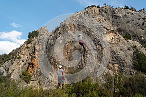 Climbing belayer boy with all the climbing gear next to a low rock wall rappelling the girl who just climbed the wall