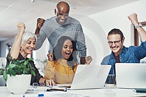 Climbing the ladder of success. a group of cheerful businesspeople looking at a laptop screen together while cheering in