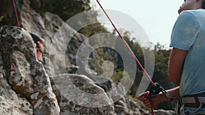 Climbing partner securing rope, outdoor teamwork on rocky terrain.