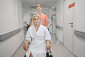 Clinic employee carries beautiful woman in wheelchair along hospital corridor