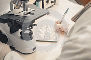 Clinical analyst writing down the results of a laboratory sample examined under a microscope