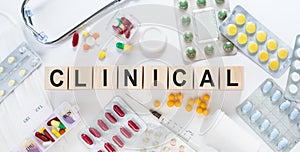 CLINICAL medicine word on wooden blocks on a desk. Medical concept with pills, vitamins, stethoscope and syringe on the background