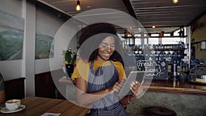 Clip of beautiful woman making decisions while holding tablet, leaning on counter of trendy coffee shop.