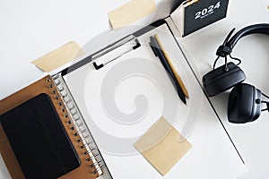 Clip folder with paper next to notepads, calendar, stickers, pens and black headphones