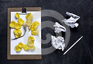 Clipboard with and aPetals of yellow rose on black background. V