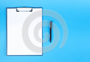 Clipboard with blank sheet of white paper and pen on blue background, place for text.