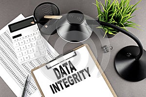 Clipboard ,chart and calculator, lamp and workspace accessories on a grey table. Top view , text DATA INTERGITY