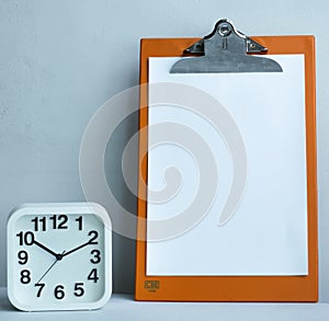 Clipboard with copy space and alarm clock on on the table.