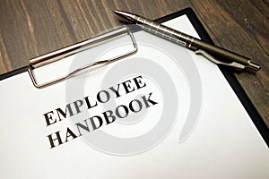 Clipboard with employee handbook and pen on desk