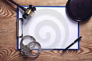 Clipboard, handcuffs, pen with judge gavel on wooden background