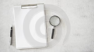 Clipboard magnifying glass and pen on white table