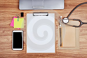 Clipboard with office supplies and stethoscope on wooden table, top view