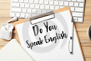 Clipboard with question Do You Speak English and stationery on wooden table, flat lay