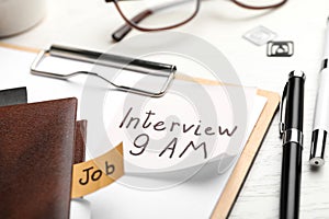 Clipboard with reminder note about job interview and stationery on table