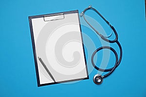 Clipboard, stethoscope and pen on blue background, flat lay