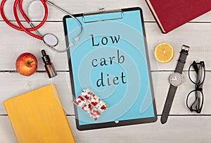 clipboard with text & x22;Low carb diet& x22;, stethoscope, books, pills, fruits, eyeglasses and watch