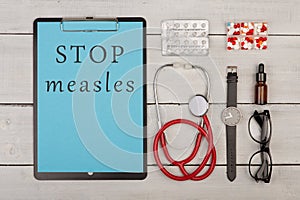 clipboard with text & x22;Stop measles& x22;, pills, stethoscope, eyeglasses and watch