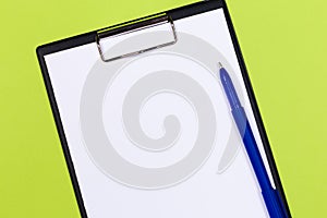 Clipboard with white sheet and pen on a green background. View from above. space for text