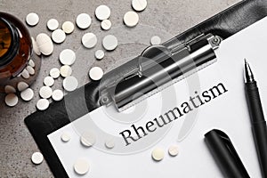 Clipboard with word Rheumatism and pills on light gray textured background, flat lay