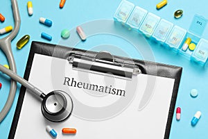 Clipboard with word Rheumatism, stethoscope and pills on light blue background, flat lay