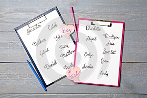 Clipboards with different baby names and felt tip pens on grey wooden table, flat lay photo