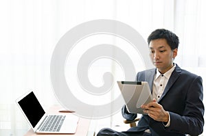 Clipping Path Handsome young asian businessman wearing suit and work with touchpad while sitting on the couch in office. Work