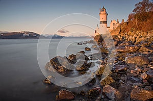 Cloch lighthouse in Scotland with long exposure of water across the rocky shore at sunset
