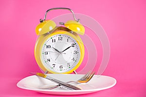 Clock with alarm and empty plate with knife and fork. Chrono diet concept photo