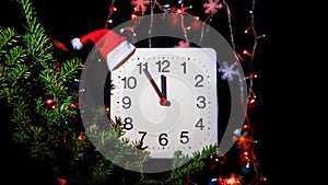 Clock in branches of New Year`s fir on black background. Second hand moves in circle of mechanical clock and show Twelve o`clock a