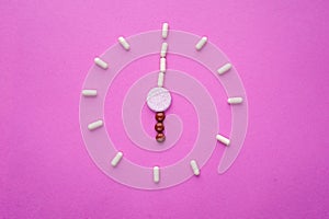 Clock created from white pills and brown tablets on pink background. Right time for using medicines