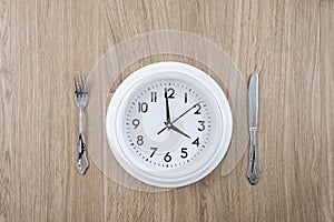 Clock with a knife and fork on a wooden background