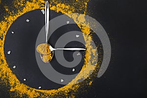 A clock made of spices and spoons on a black background.