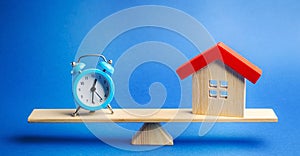 A clock and a miniature house on the scales. Mortgage and loan concept. Real estate and risks. Property insurance. Credit. Tax