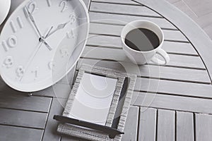 Clock, notebook and a cup of coffee on wooden table.