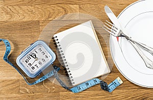 Clock, notebook, tape measure and dish with cutlery on a wooden background