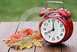 Clock with orange autumn leaves, daylight savings time concept