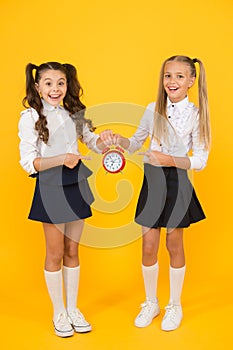 This clock is perfect. Happy little girls pointing at vintage alarm clock on yellow background. Small school children