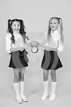 This clock is perfect. Happy little girls pointing at vintage alarm clock on yellow background. Small school children