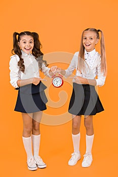 This clock is perfect. Happy little girls pointing at vintage alarm clock on yellow background. Small school children
