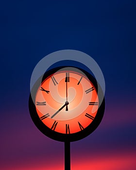 a clock with roman numerals on it against a red sky