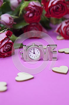 A clock in the shape of a word of love. On a pink background, hearts and flowers of roses. The concept of valentines day, wedding