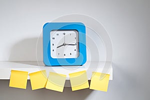 A clock on the shelf with many empty sticky notes.