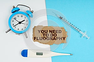 A clock, a thermometer, a syringe and a cardboard with the inscription - You need to do fluography