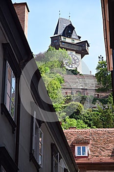 Clock tower in Graz on top of the hill, above the roofs, above the large stone walls, seen from an alley.