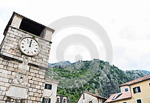 Clock tower in the Square of the Arms, with the mountains in the background. Kotor, Montenegro. Stone architecture building in old