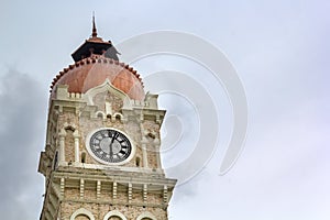 Clock on an urban stone tower against a gray sky with clouds.