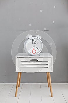 Clock on a white nightstand near gray wall