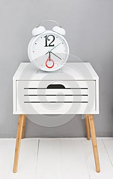 Clock on a white nightstand near gray wall